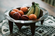 Close-up of a decorative centerpiece bowl filled with fresh seasonal fruits on a wooden table runner.