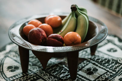 A rustic terracotta bowl filled with fresh fruit, sitting on a wooden table.