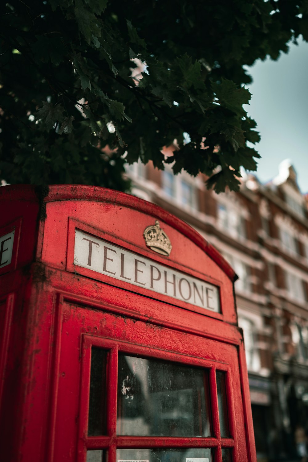 a red telephone booth sitting next to a tree