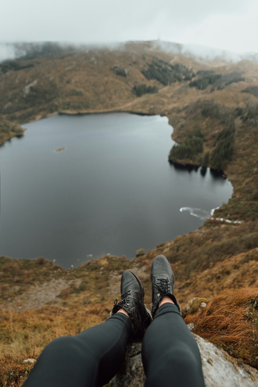 person sitting on rock facing the lake during day