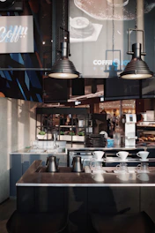 A sleek modern office breakroom featuring neatly arranged coffee machines, snack displays, and minimalist decor in black, white, and gold tones.