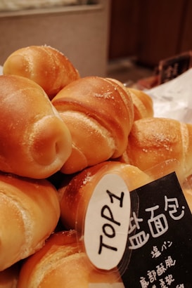 A close-up view of several freshly baked bread rolls with a golden-brown crust, piled together. A label with bold text 'TOP1' is attached to the bread with additional writing in another language, possibly indicating the bread's ranking or type.