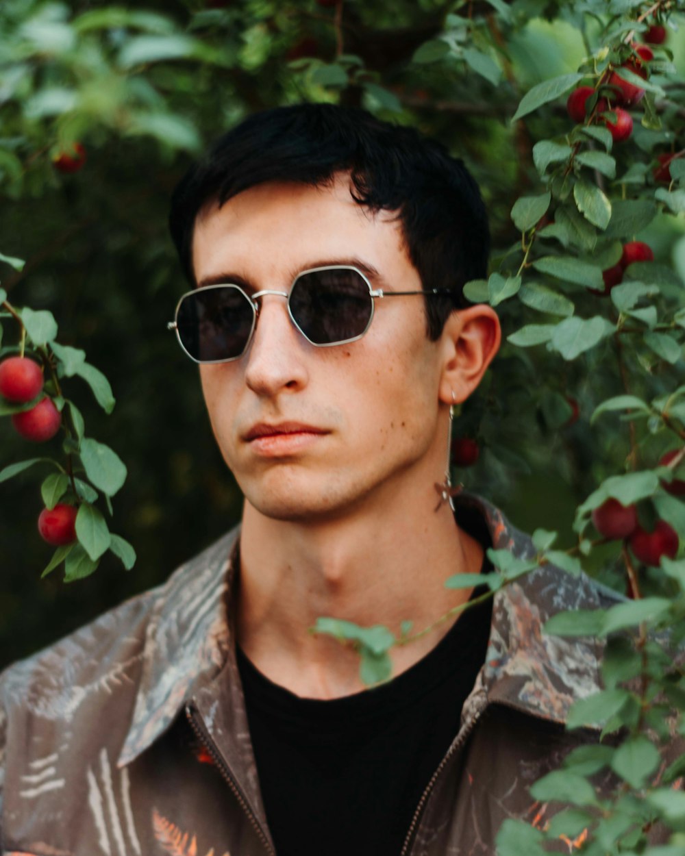 a man wearing sunglasses standing in front of a tree