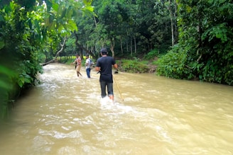 A group crossing a shallow river together, supporting each other carefully.