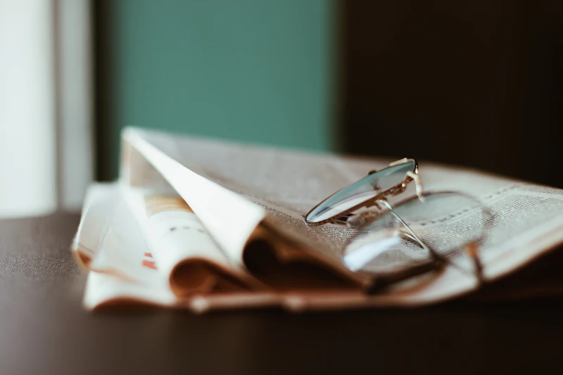 Reading glasses on a folded newspaper beside a soft green wall
