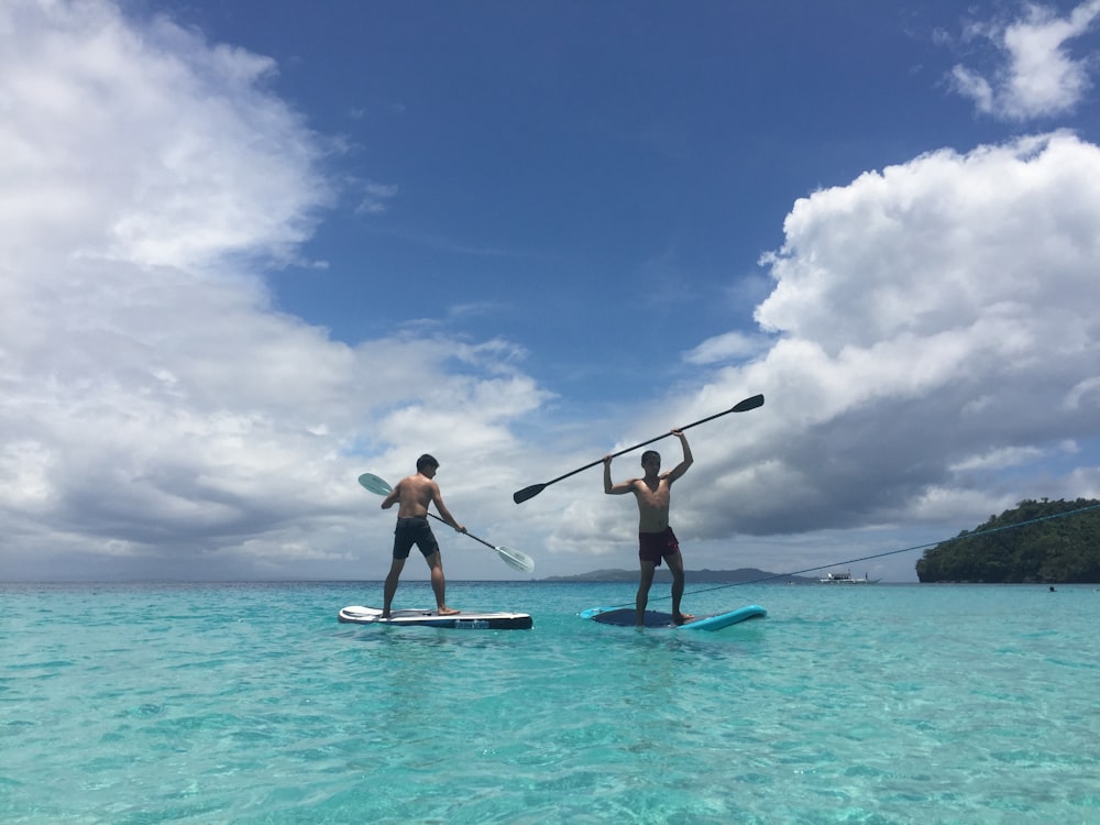 two men standing on blue and white paddle boards