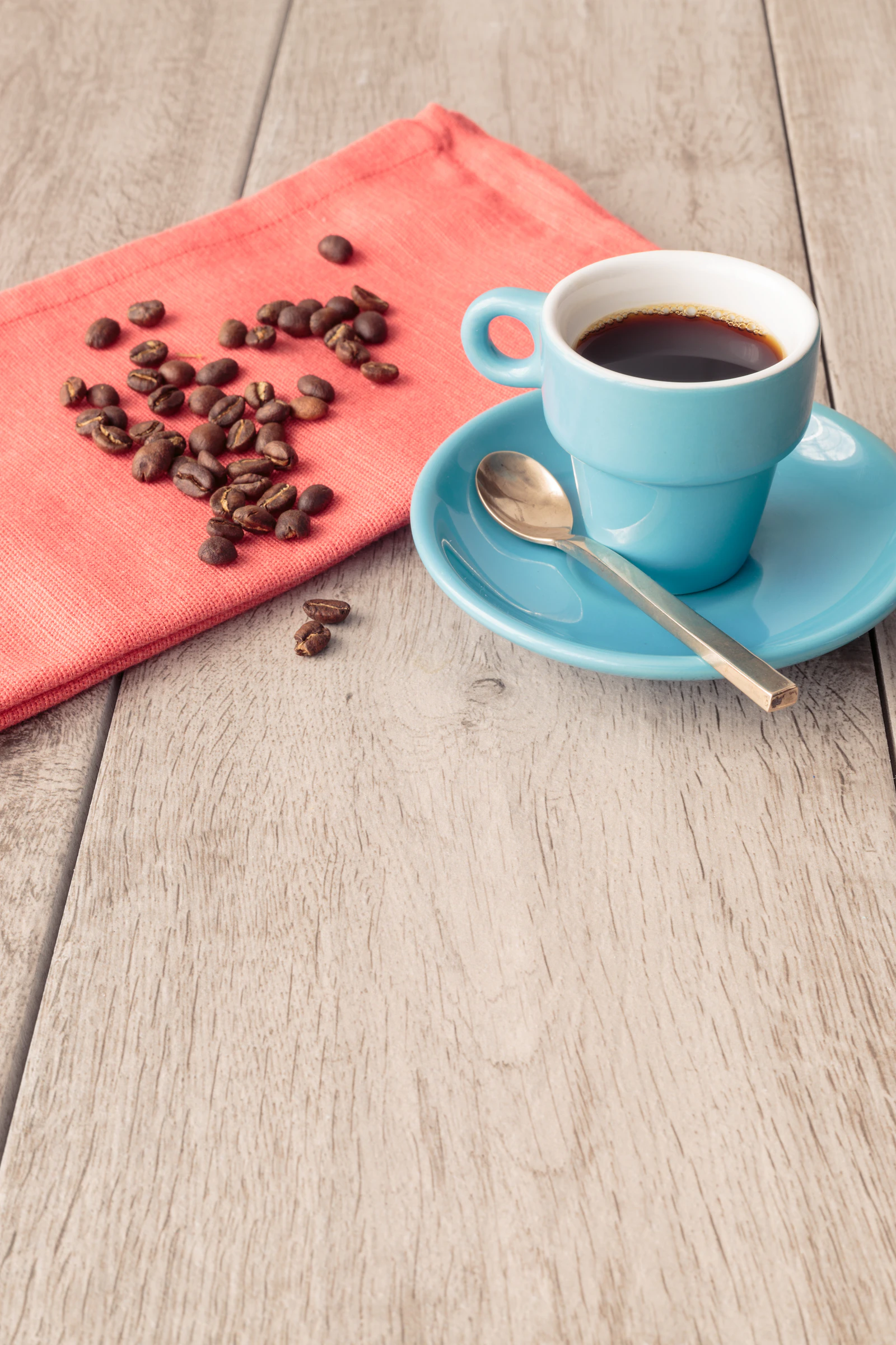 A small blue cup of black coffee sits beside scattered beans on a bright table.