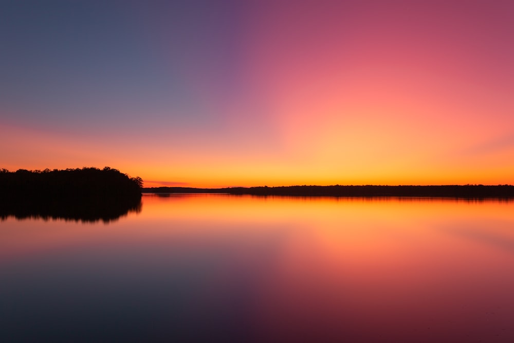 silhouette d’arbres se reflétant sur l’eau calme pendant l’heure dorée