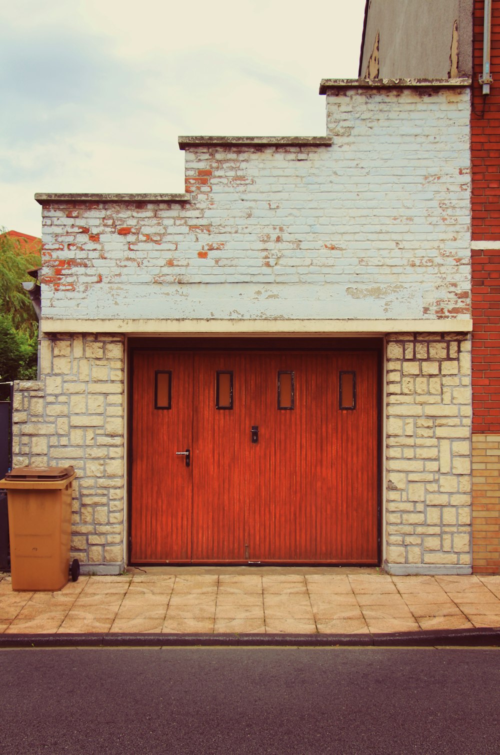 a brick building with a red door and a trash can