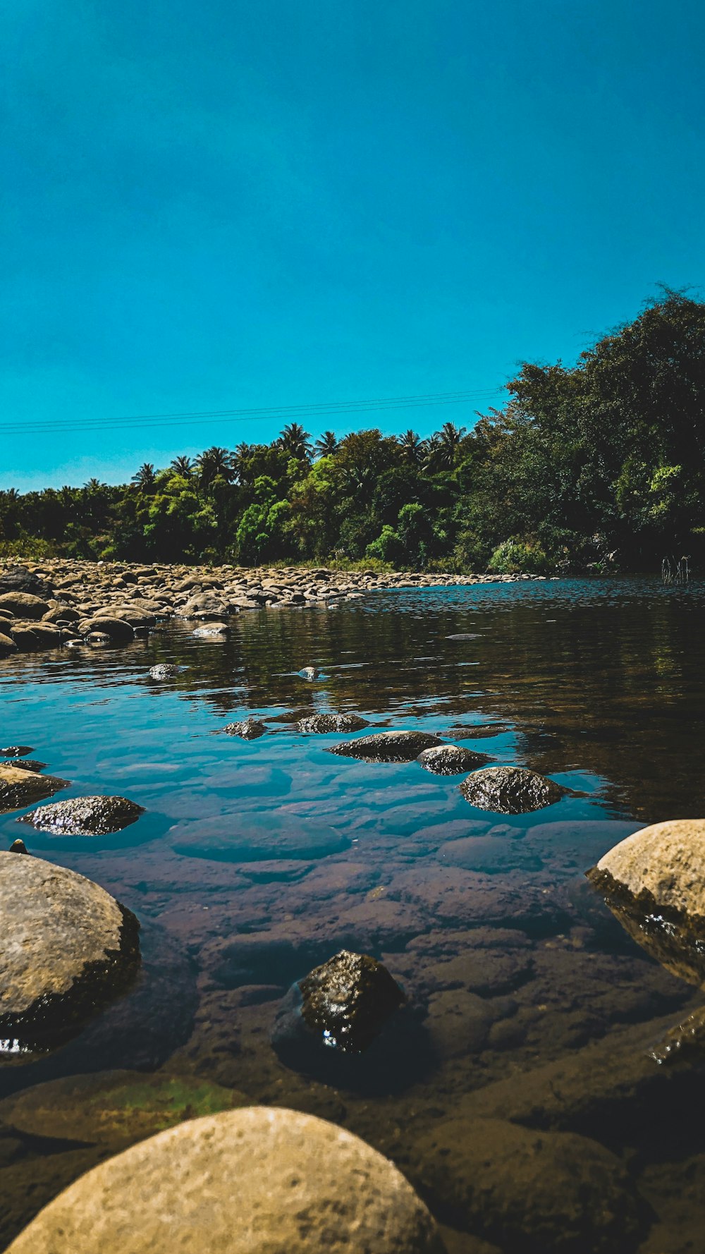 body of water near stones under clear sky