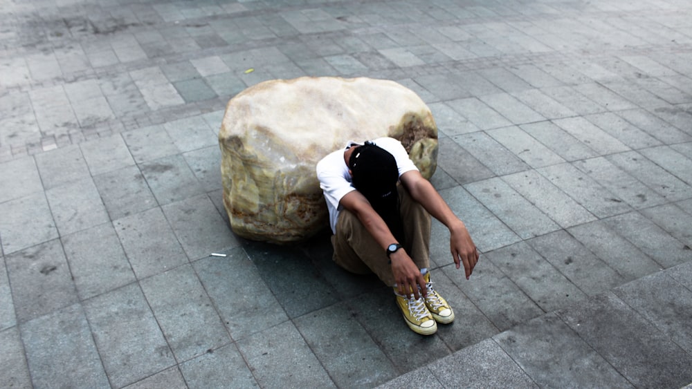 person looking down while siting on concrete pathway during daytime