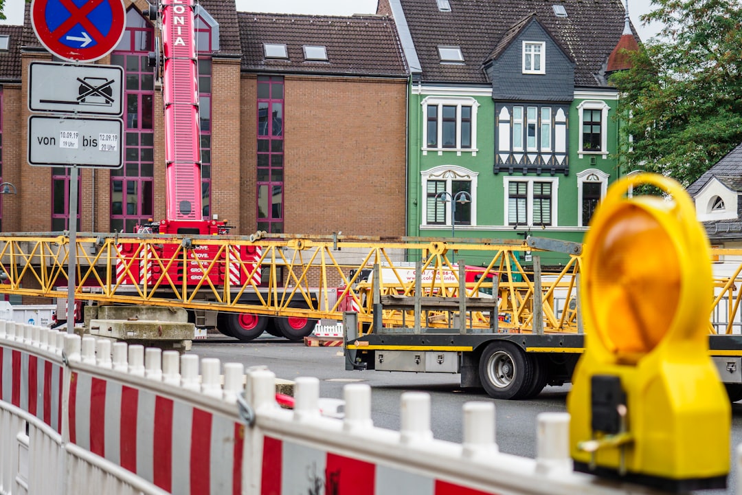 truck loads yellow crane at the back near building