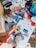 A collection of old and discarded media items including several cassette tapes, CDs, and a VHS tape scattered on the ground. There's also some cardboard packaging, torn paper, and a variety of litter among the items, suggesting a disorganized and neglected area.
