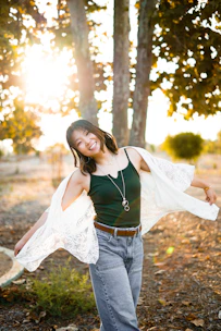 A woman wearing a soft pastel t-shirt, smiling outdoors with sunlight filtering through trees.