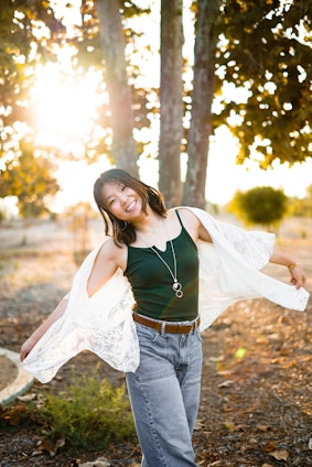 A stylish adult woman wearing a cozy sweater and jeans, smiling outdoors on a sunny day
