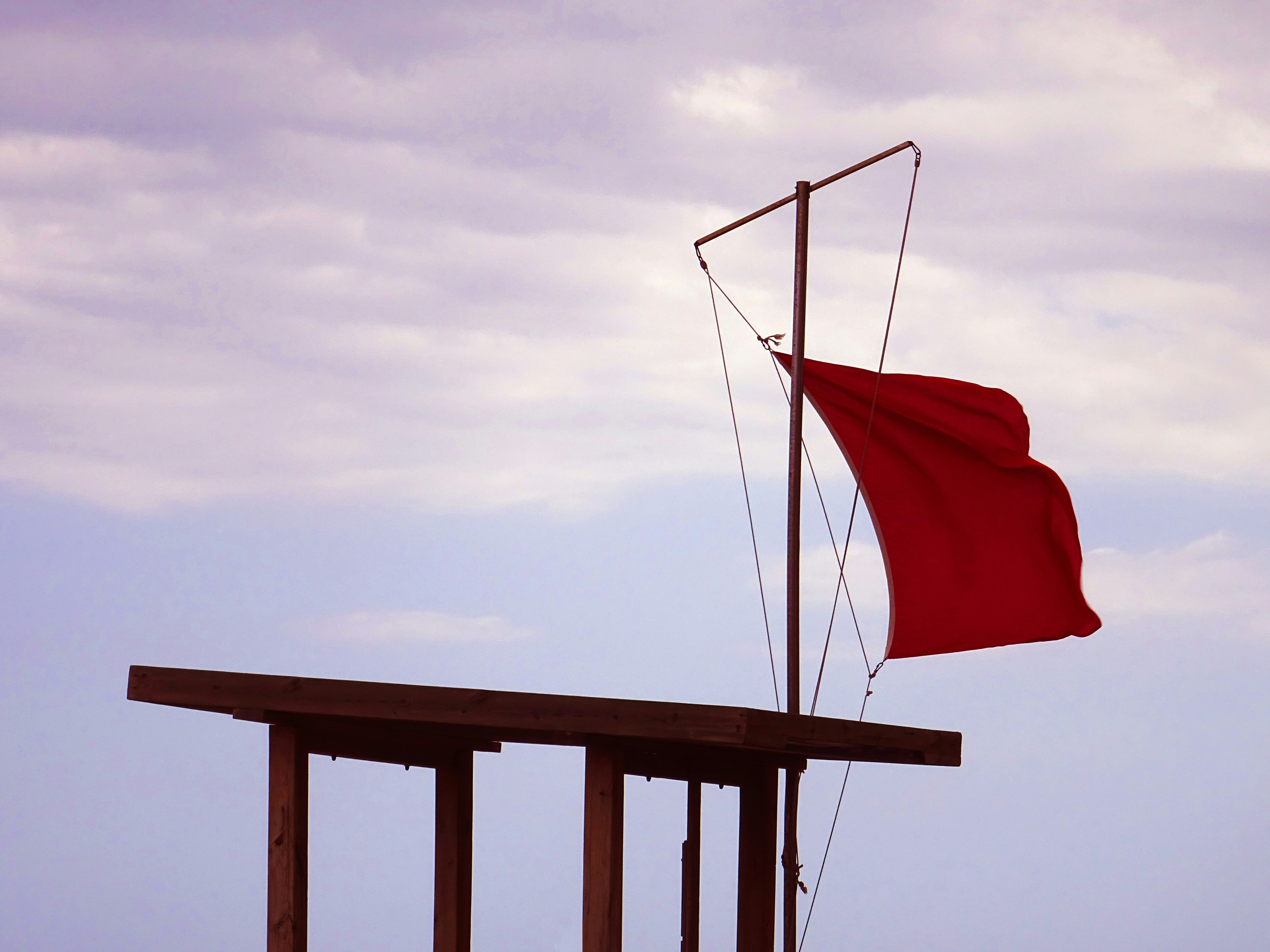 Red flag on a beach at a lifeguard tower with a cloudy sky.