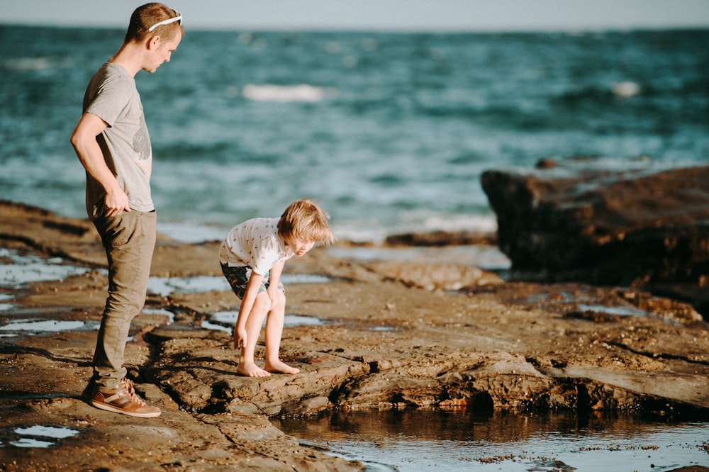 boy and man standing on rock during daytime