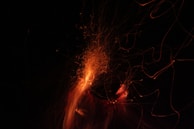 Sparks and wisps of orange light dance against a dark background, creating a mesmerizing display of motion and energy. The streaks of light appear vibrant and dynamic, capturing the essence of fire or glowing embers.