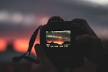 Close-up of a camera lens capturing a dramatic sunset over a city skyline.