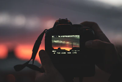 Close-up of a photographer holding a camera, capturing a vibrant cityscape at sunset.