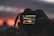 A close-up of a photographer capturing a vibrant sunset with a camera.