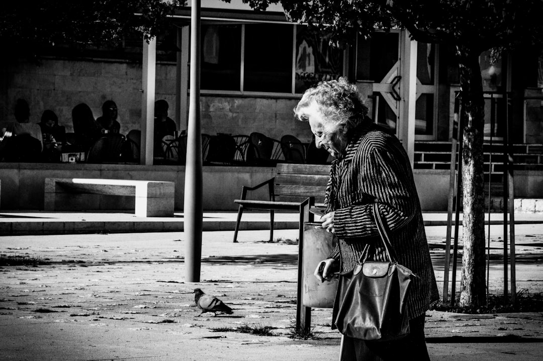 grayscale photography of woman walking on street holding handbag