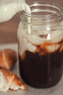 Freshly made doce de leite being poured slowly into a glass jar in a cozy kitchen setting.