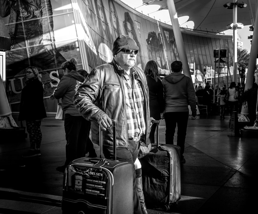 grayscale photo of standing man between luggage bags