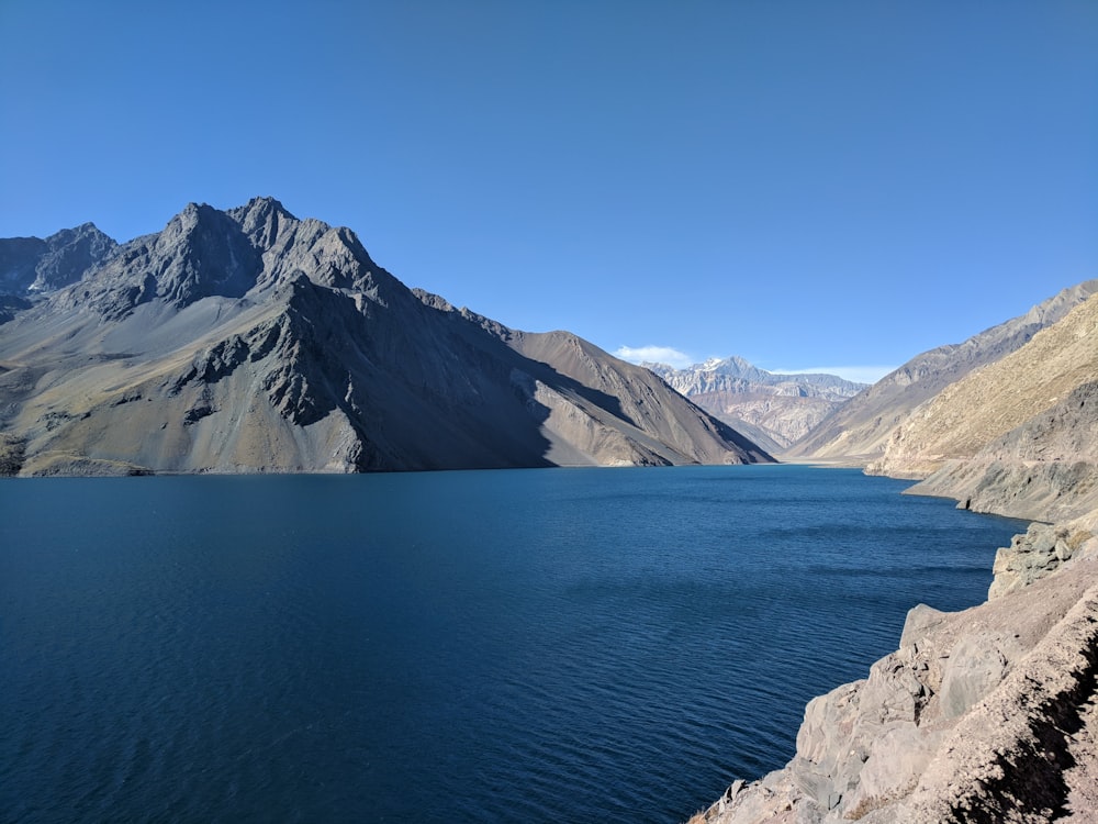 blue body of water surrounded by mountains under blue sky