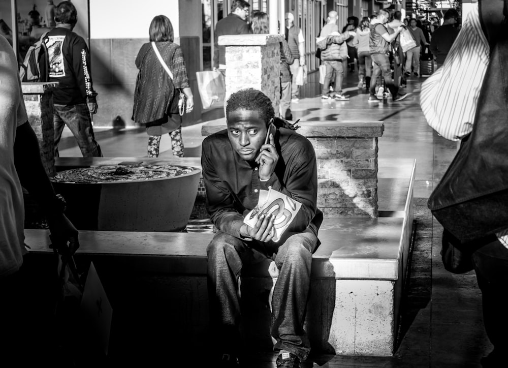 grayscale photography of man sitting beside crowd of peple