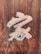 A wooden surface featuring a carved artistic symbol with a combination of light blue and beige colors. The background shows detailed wood grain textures, and there is a small stamp or seal in the bottom right corner.