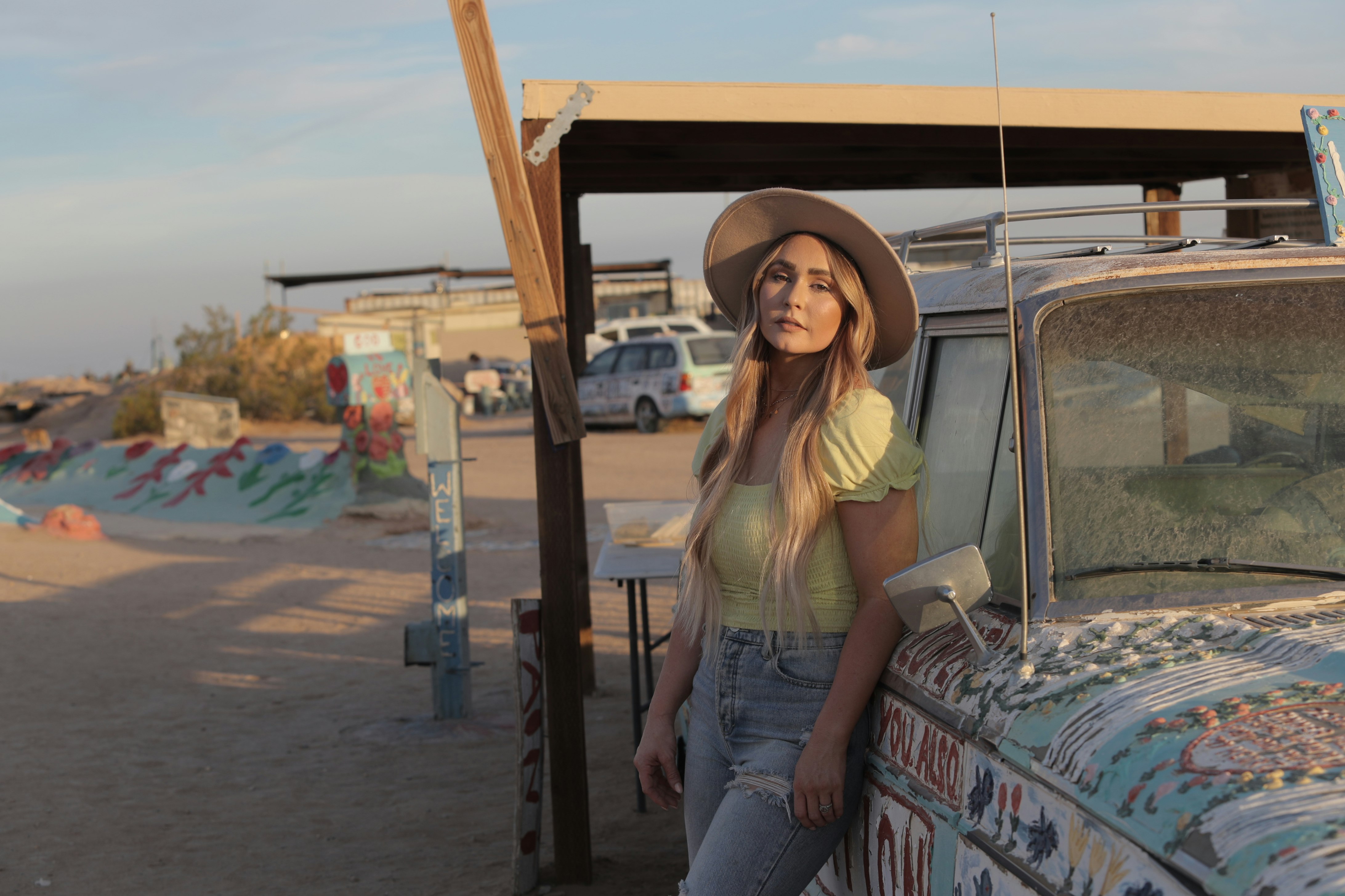 woman wearing yellow cap-sleeved blouse leaning on car