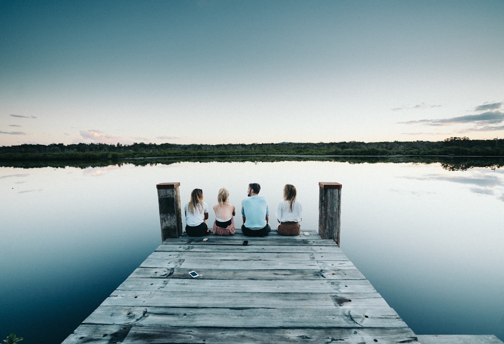 three people sitting on a dock looking out at the water