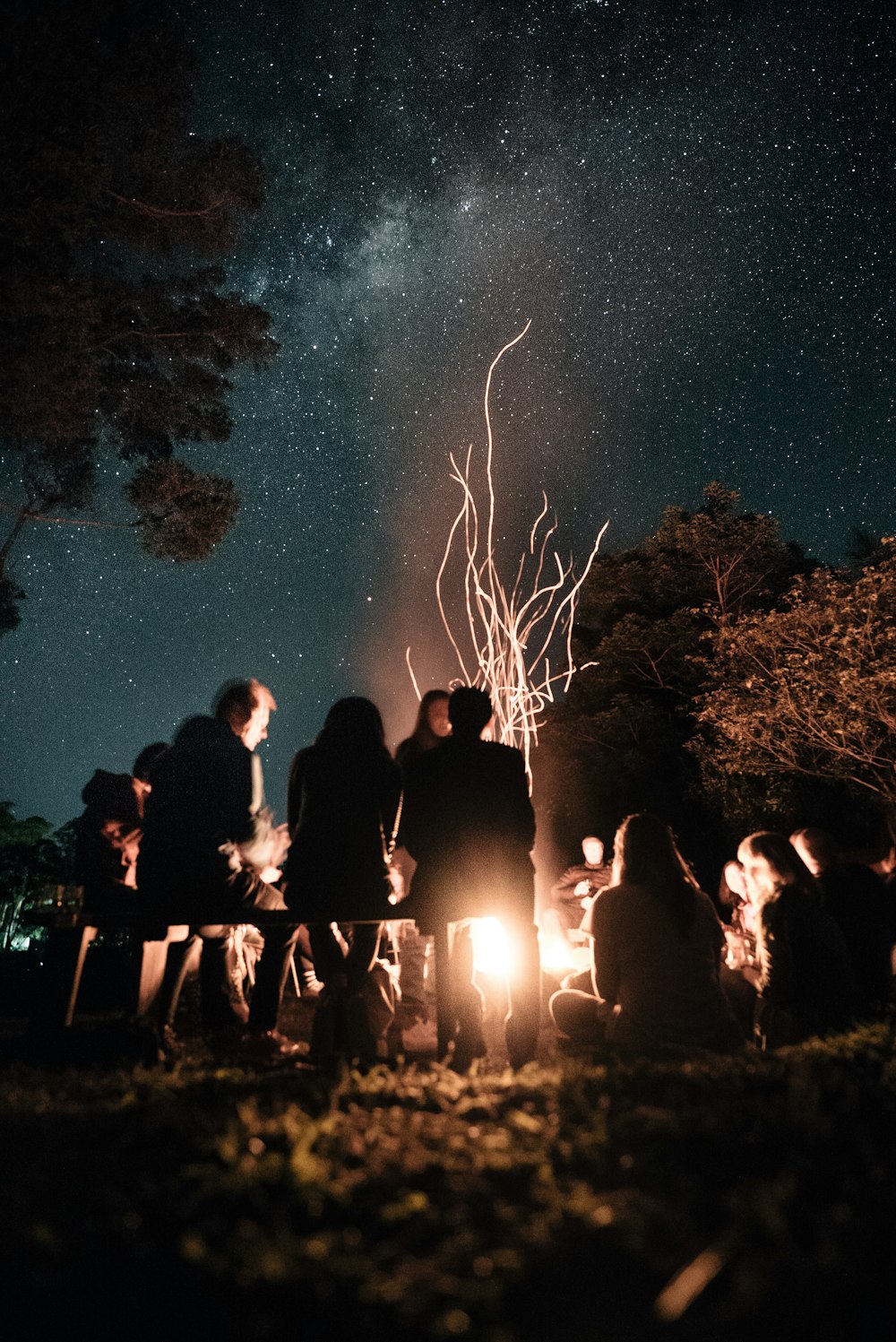 夜にキャンプファイヤーの周りに座っている人々のグループ