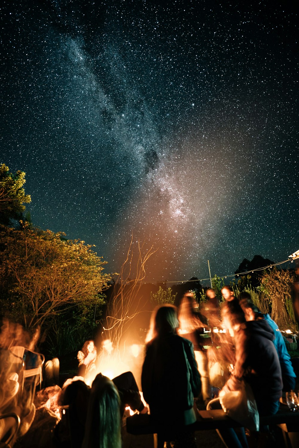 a group of people sitting around a campfire under a night sky filled with stars