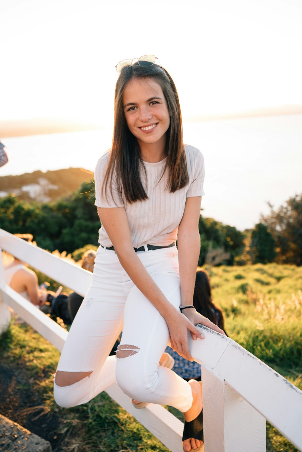 woman wearing white ripped skinny jeans sitting on white metal fence