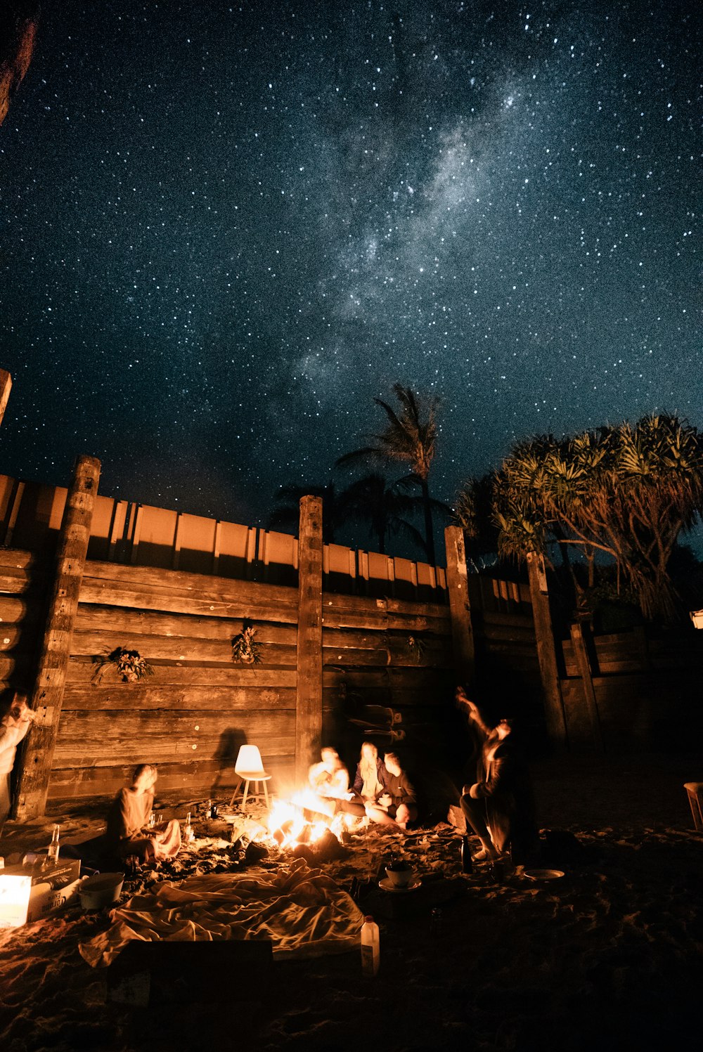 a group of people sitting around a campfire under a night sky filled with stars