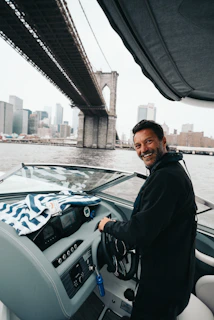 Close-up of a smiling fleet member steering an electric boat with the coastline in the background.