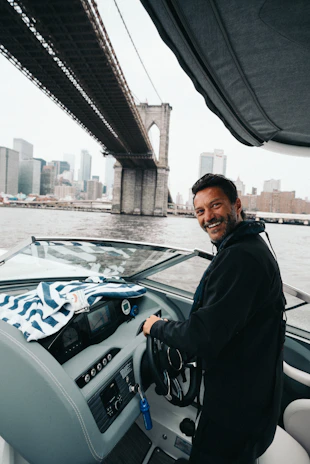 Close-up of a smiling fleet member steering an electric boat with the coastline in the background.