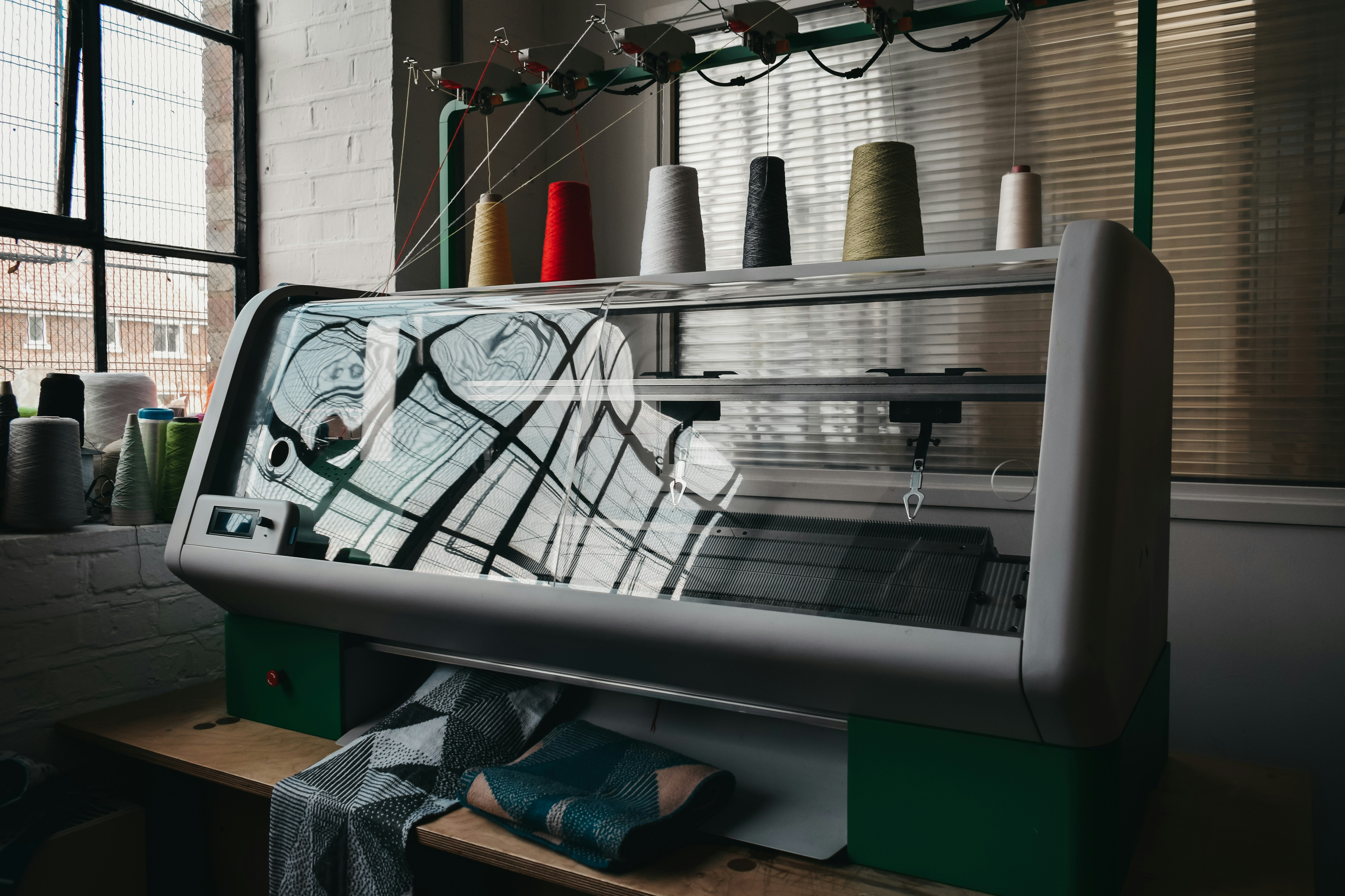 Industrial knitting machine surrounded by colorful yarn and fabric swatches.