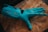 A robotic hand in a bright teal color lies on a textured wooden surface. The design of the hand includes articulated joints and slits on each finger, suggesting functionality and mechanical sophistication.