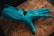 A robotic hand in a bright teal color lies on a textured wooden surface. The design of the hand includes articulated joints and slits on each finger, suggesting functionality and mechanical sophistication.