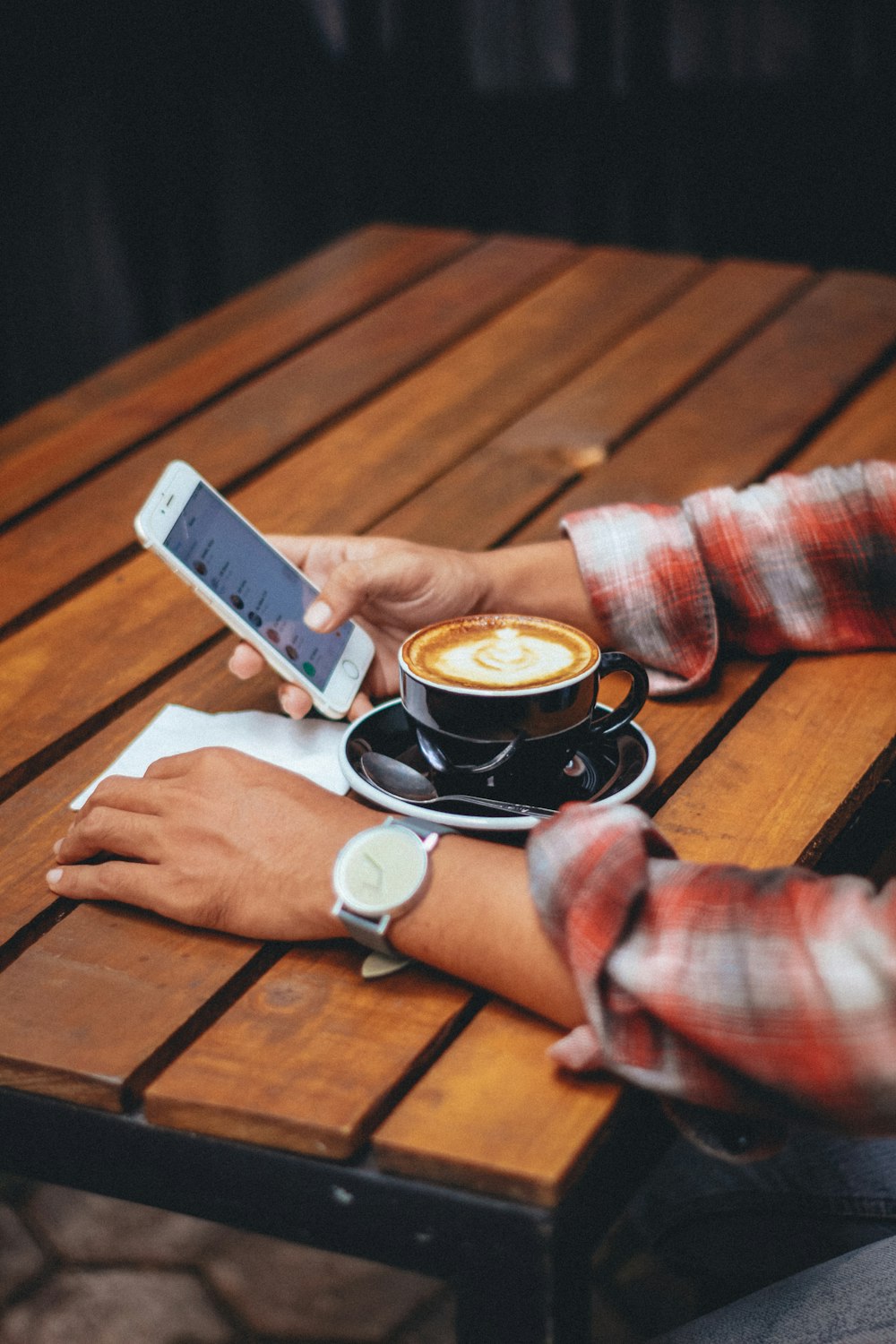 person holding gold iPhone with teacup on table