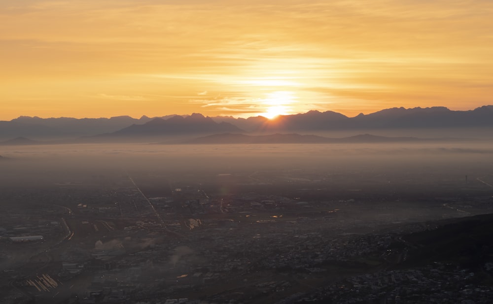 the sun is setting over a city with mountains in the background