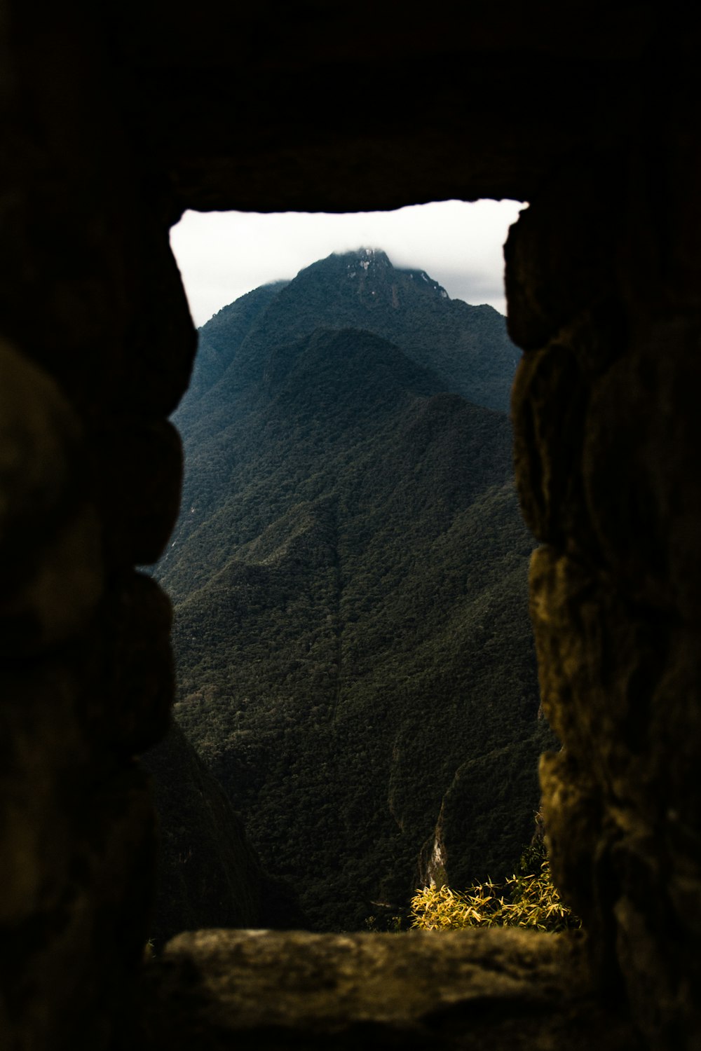 a view of mountains through a window in a stone wall