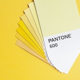 A set of color swatches fanned out on a yellow background, featuring various shades of yellow and labeled 'Pantone 600' on the top card.