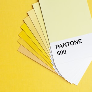 A set of color swatches fanned out on a yellow background, featuring various shades of yellow and labeled 'Pantone 600' on the top card.