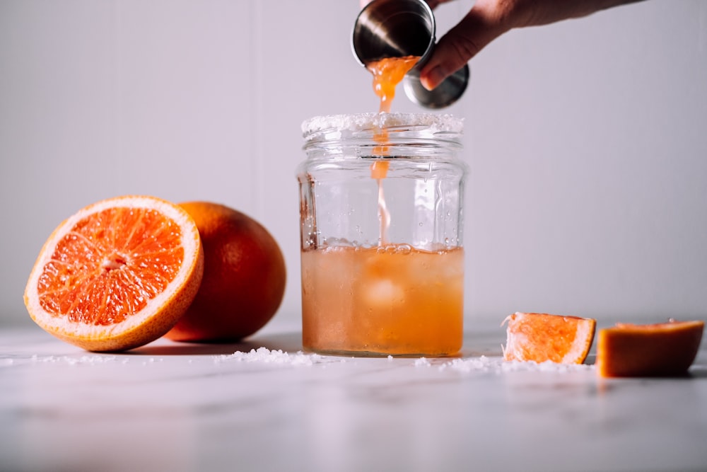 une personne verse un liquide sur un bocal près des fruits oranges