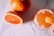 A refreshing orange beverage with ice and a salt rim sits beside whole and sliced oranges on a light-colored surface. The drink garnished with a slice of orange peel creates a vibrant and summery atmosphere.