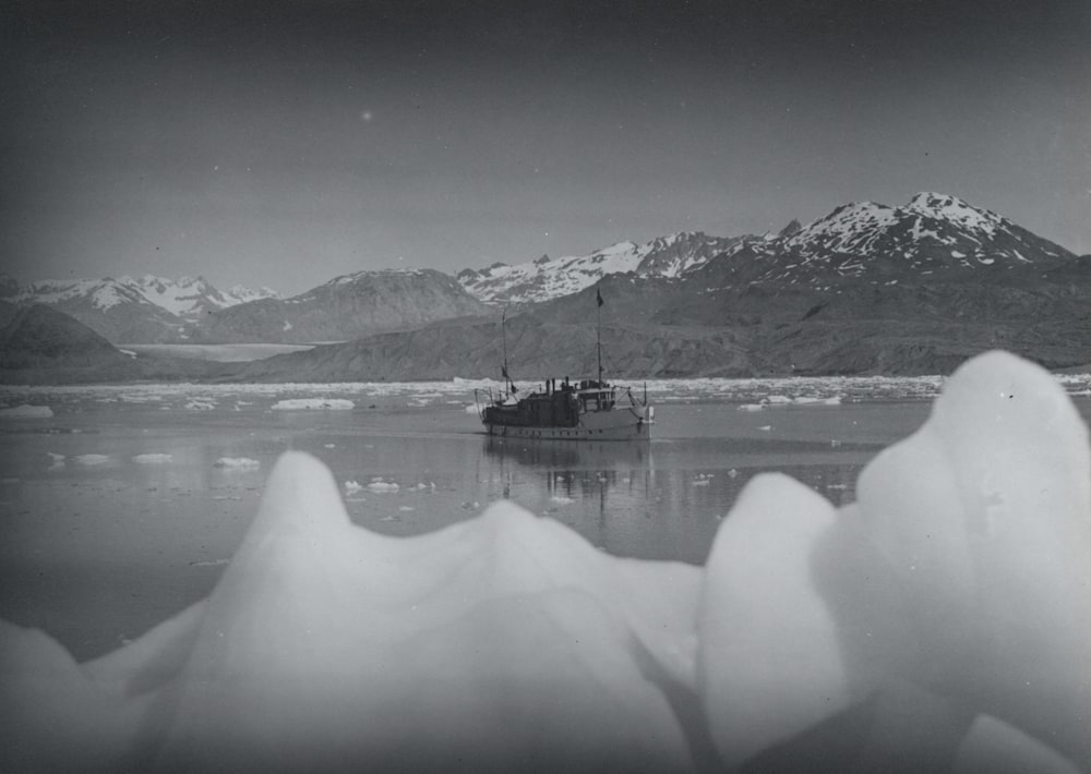 grayscale photo of boat near mountain